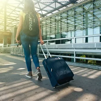 Eine Frau in gelbem T-Shirt, die auf dem Weg zum Flughafen Terminal ist und einen Koffer hinter sich herträgt.